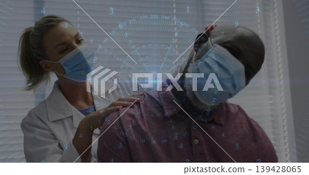 Assessing clinician examining seated man neck shoulders in clinic, coat blue masks maroon polo HUD 139428065