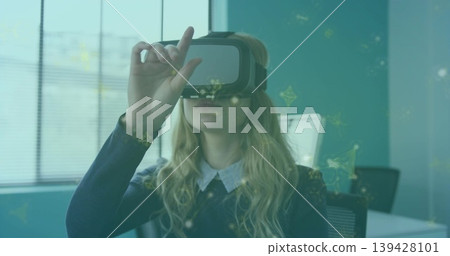 Adjusting woman in collared shirt dark sweater using VR headset at desk, AR overlays 139428101