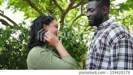 Smiling couple touching hair and gazing in backyard under tree, in plaid shirt, olive green top Smiling couple touching hair and gazing in backyard under tree, in plaid shirt, olive green top 139428179