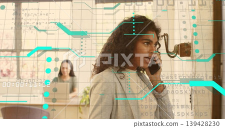 Talking woman in blazer holding phone near wall phone in office, coworker working laptop with HUD Talking woman in blazer holding phone near wall phone in office, coworker working laptop with HUD 139428230