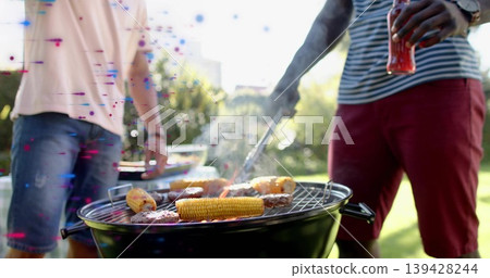 Grilling two men flipping burgers and corn on charcoal grill in backyard, holding metal tongs Grilling two men flipping burgers and corn on charcoal grill in backyard, holding metal tongs 139428244