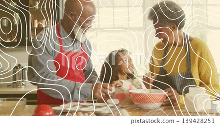 Stirring senior couple and granddaughter at home kitchen, wearing aprons and using red mixing bowl 139428251