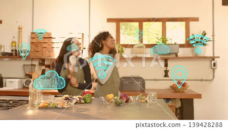 Laughing two women in green aprons preparing meal at home, holding wooden spoon, AR icons appearing Laughing two women in green aprons preparing meal at home, holding wooden spoon, AR icons appearing 139428288