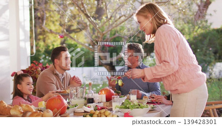 Serving pink-sweatered woman passing dish on covered porch with dining table, man in brown sweater 139428301