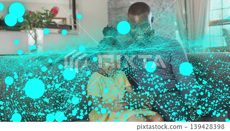 Sitting father in dark top with daughter in yellow dress on sofa, turquoise particle overlay 139428398