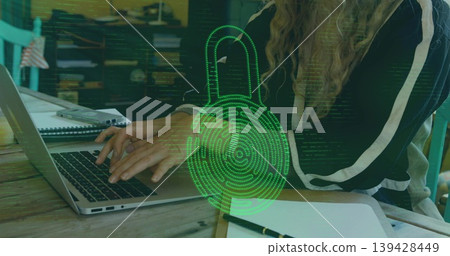 Typing woman in dark striped top at wooden table, using laptop, notebook, green padlock overlay Typing woman in dark striped top at wooden table, using laptop, notebook, green padlock overlay 139428449