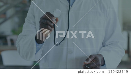Holding metal stethoscope, senior doctor presenting torso in clinic, wearing white lab coat and tie Holding metal stethoscope, senior doctor presenting torso in clinic, wearing white lab coat and tie 139428549