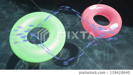 Floating neon green and pink rings, white handles on dark pool casting purple or blue trails, causti Floating neon green and pink rings, white handles on dark pool casting purple or blue trails, causti 139428640