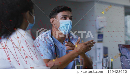 Gesturing man in light blue scrubs discussing patient data at hospital meeting area, with laptop Gesturing man in light blue scrubs discussing patient data at hospital meeting area, with laptop 139428650