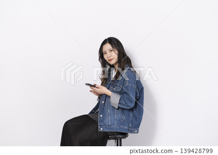 一位年輕女子坐在椅子上操作手機 一位年輕女子坐在椅子上操作手機 139428799