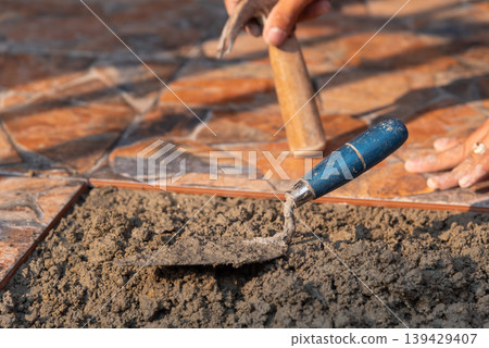 Close up of worker installing floor tiles using trowel and cement mortar construction process renovation flooring work detail tools and materials Close up of worker installing floor tiles using trowel and cement mortar construction process renovation flooring work detail tools and materials 139429407
