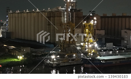 A global maritime grain terminal with massive concrete silos, illuminated yellow cranes, and the bulk carrier ship docked for loading under floodlights A global maritime grain terminal with massive concrete silos, illuminated yellow cranes, and the bulk carrier ship docked for loading under floodlights 139430183