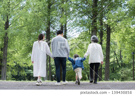 A happy family life: a three-generation family holding hands while walking through a park amidst fresh greenery; a full-body shot with no faces visible. A happy family life: a three-generation family holding hands while walking through a park amidst fresh greenery; a full-body shot with no faces visible. 139430858