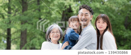 A three-generation family's smiling, camera-facing portrait; a close-up of their upper bodies capturing their happy family life in a park surrounded by fresh greenery. 139430866