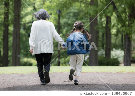 A grandmother playing in a park surrounded by fresh spring greenery, and her smiling granddaughter walking beside her. (Full body shot, back view, face not shown) A grandmother playing in a park surrounded by fresh spring greenery, and her smiling granddaughter walking beside her. (Full body shot, back view, face not shown) 139430967