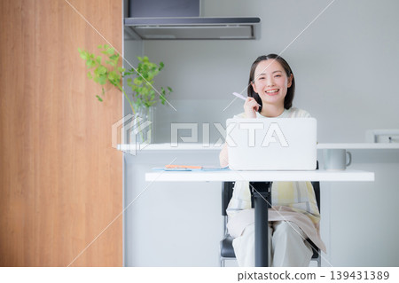 一位面帶微笑的女士在餐廳裡用筆記型電腦工作;她是一位遠距工作者;在家工作或在家學習以獲得資格證書的女士。 一位面帶微笑的女士在餐廳裡用筆記型電腦工作;她是一位遠距工作者;在家工作或在家學習以獲得資格證書的女士。 139431389