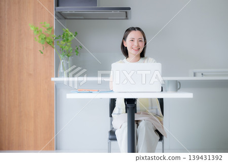 一位面帶微笑的女士在餐廳裡用筆記型電腦工作;她是一位遠距工作者;在家工作或在家學習以獲得資格證書的女士。 一位面帶微笑的女士在餐廳裡用筆記型電腦工作;她是一位遠距工作者;在家工作或在家學習以獲得資格證書的女士。 139431392