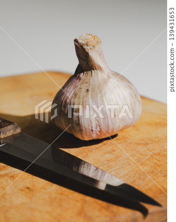 Whole garlic bulb and kitchen knife on a wooden cutting board Whole garlic bulb and kitchen knife on a wooden cutting board 139431653