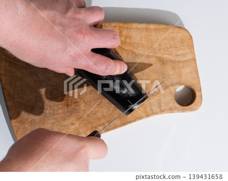 Hands slicing dark eggplant on wooden cutting board with a knife Hands slicing dark eggplant on wooden cutting board with a knife 139431658