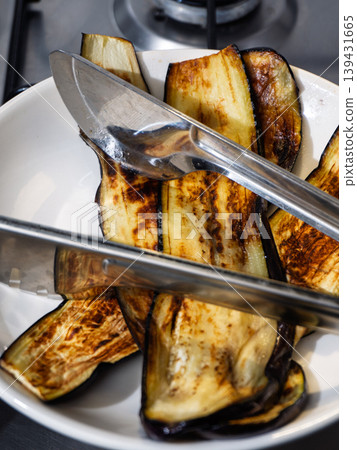 Grilled eggplant slices in a white bowl with stainless steel tongs Grilled eggplant slices in a white bowl with stainless steel tongs 139431665