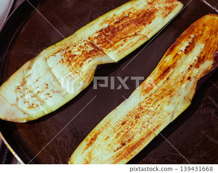 Two long eggplant slices frying in a dark pan until golden brown Two long eggplant slices frying in a dark pan until golden brown 139431668