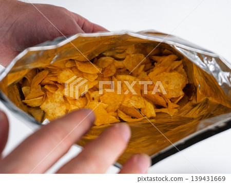 Hands holding open a foil bag filled with golden potato chips Hands holding open a foil bag filled with golden potato chips 139431669