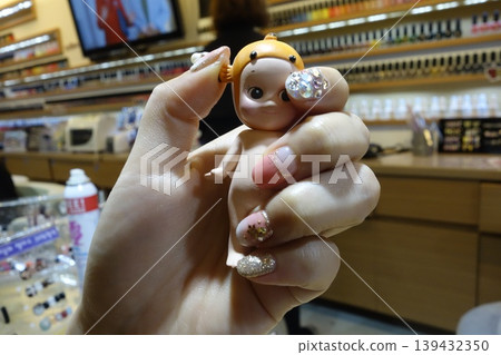 Hand with Glitter Nail Art Holding Doll in Store Hand with Glitter Nail Art Holding Doll in Store 139432350