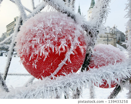 Winter's Icy Touch: Close-up of two vibrant red spheres encased in delicate frost crystals, creating a stunning contrast against the blurred city backdrop. A celebration of winter. 139433258