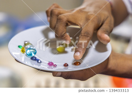 A close-up view of a hand carefully sorting and examining a collection of colorful, polished gemstones on a white ceramic plate. Sri Lanka island in Asia. 139433313