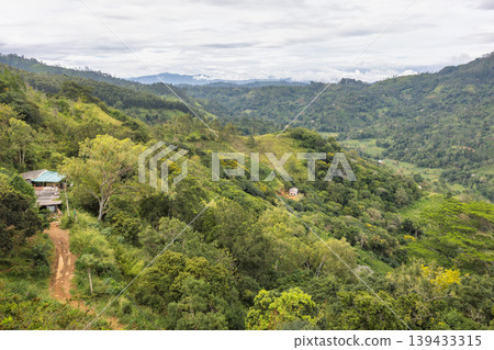 Verdant Mountain Landscape with Scattered Dwellings Under a Cloudy Sky, Reflecting Serenity and Nature's Grandeur. Mountain landscape near Ella town in Sri Lanka island in Asia. Verdant Mountain Landscape with Scattered Dwellings Under a Cloudy Sky, Reflecting Serenity and Nature's Grandeur. Mountain landscape near Ella town in Sri Lanka island in Asia. 139433315