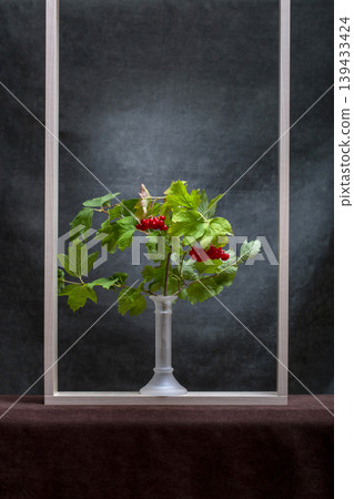 A branch of red viburnum in a vase and a wooden frame A branch of red viburnum in a vase and a wooden frame 139433424