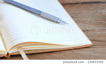 A notebook and pen placed on a wooden desk. A notebook and pen placed on a wooden desk. 139433563
