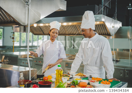 Culinary students practicing cooking together in modern training kitchen preparing food with teamwork Culinary students practicing cooking together in modern training kitchen preparing food with teamwork 139434384