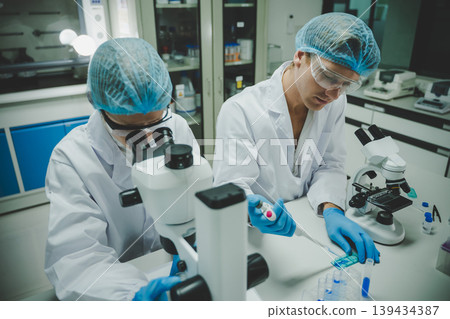 Researchers in laboratory environment using pipette and microscope for medical chemistry and biology research highlighting accuracy discovery and innovation 139434387