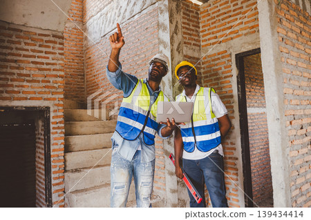 Two Black engineers reviewing construction documents and tools at building site Two Black engineers reviewing construction documents and tools at building site 139434414