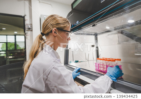 Female scientist working with test tubes inside laminar flow hood in sterile laboratory environment 139434425