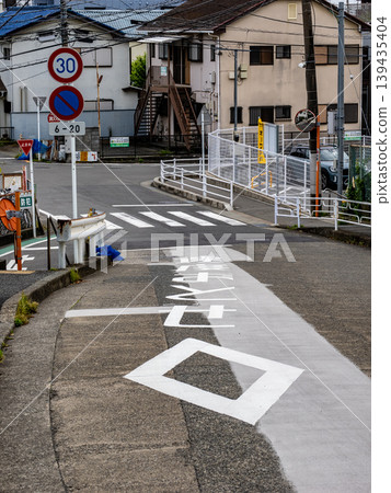 Road markings on a downhill slope: a diamond symbol indicating a pedestrian crossing and the words "Slow down." 139435404