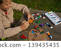A child decorating flat pebbles with acrylic paint, depicting fresh produce like apples, carrots, and tomatoes. 139435435