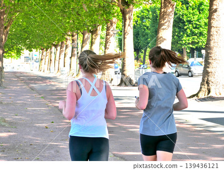 Two women running along a tree-lined street. 139436121