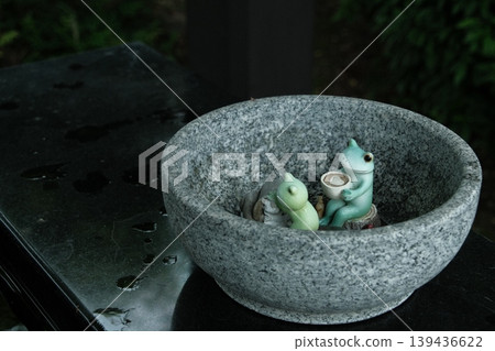 A frog figurine relaxing in a stone water basin – a soothing interior decoration. A frog figurine relaxing in a stone water basin – a soothing interior decoration. 139436622