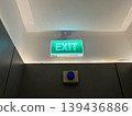 Green emergency exit sign glowing above the door in a dark office building hallway. Safety symbol for evacuation route, fire exit guidance, and concept of finding a way out or solution 139436886