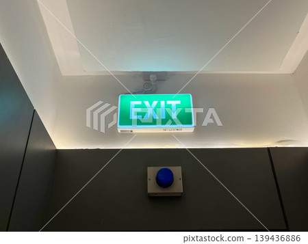 Green emergency exit sign glowing above the door in a dark office building hallway. Safety symbol for evacuation route, fire exit guidance, and concept of finding a way out or solution 139436886