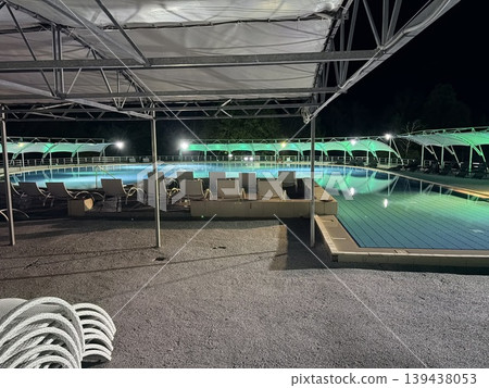 A tranquil swimming pool complex at night, illuminated by artificial lighting. 139438053