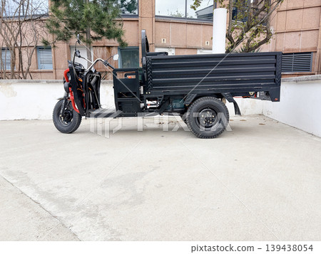 A three-wheeled electric cargo truck parked on a light-gray concrete surface. A three-wheeled electric cargo truck parked on a light-gray concrete surface. 139438054