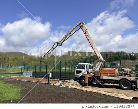 a construction scene featuring a large concrete pump truck with its articulated boom arm extended high into the air. a construction scene featuring a large concrete pump truck with its articulated boom arm extended high into the air. 139438074