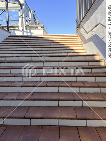 The staircase is covered with tiles and leads up to the blue sky. Conceptual symbolic photo of a copper staircase leading upwards. The staircase is covered with tiles and leads up to the blue sky. Conceptual symbolic photo of a copper staircase leading upwards. 139438085