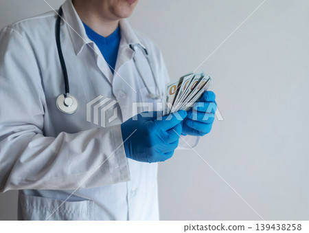 Close-up of doctor in white coat and blue gloves receiving or hiding cash. Concept of high medical salary, corruption in medicine, healthcare bribery, and expensive health insurance. Close-up of doctor in white coat and blue gloves receiving or hiding cash. Concept of high medical salary, corruption in medicine, healthcare bribery, and expensive health insurance. 139438258