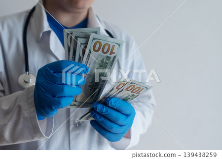 Close-up of doctor in white coat and blue gloves receiving or hiding cash. Concept of high medical salary, corruption in medicine, healthcare bribery, and expensive health insurance. Close-up of doctor in white coat and blue gloves receiving or hiding cash. Concept of high medical salary, corruption in medicine, healthcare bribery, and expensive health insurance. 139438259