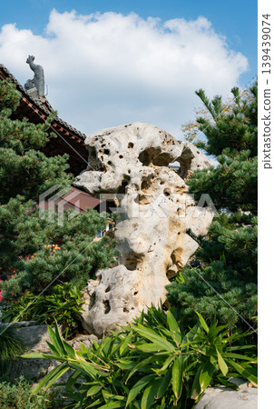 Taihu stone artfully placed among lush pines and bamboo near traditional Chinese architecture in a serene garden Taihu stone artfully placed among lush pines and bamboo near traditional Chinese architecture in a serene garden 139439074