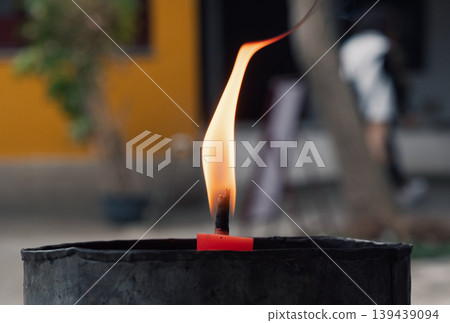 Flame burns from a candle in a holder at a street scene during daylight hours Flame burns from a candle in a holder at a street scene during daylight hours 139439094